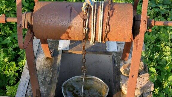 妇女把铁链和水桶扔进乡下的井里打水古老的水井链关闭锈迹斑斑的旧链条是村里的井