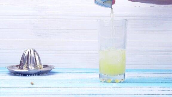 制作柠檬汁与鲜榨有机柠檬滴冰块在玻璃杯中并与水在蓝色木板上混合特写夏季概念