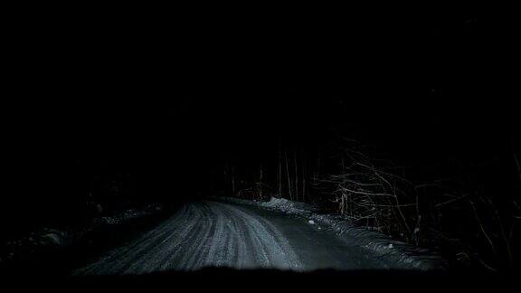 汽车夜间行驶在白雪覆盖的森林道路上