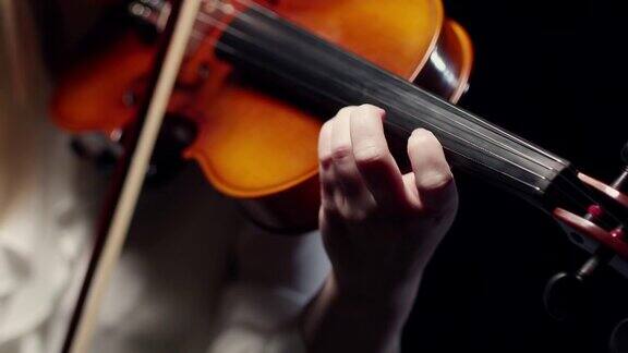 一个金发女人在拉小提琴手指在小提琴的指板上一个黑色的背景拍摄的特写