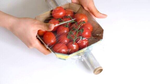 一个在白色桌子上用食物胶片储存食物的女人用于包装产品的透明聚乙烯食品薄膜一次性塑料包装的樱桃番茄近距离