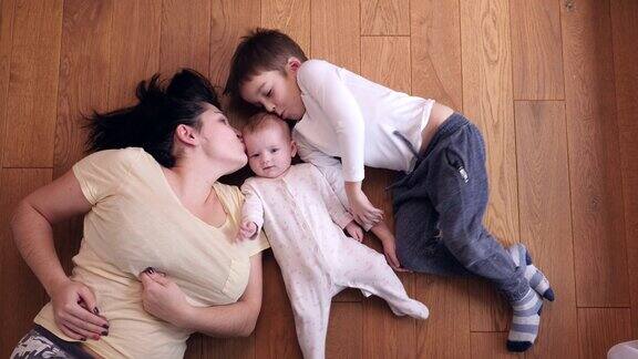 俯视图幸福的家庭母亲与儿子亲吻小妹妹躺在地板上