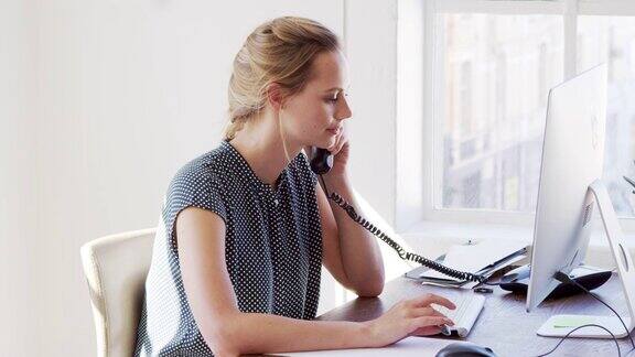 年轻的白人妇女在办公室里使用电话和电脑