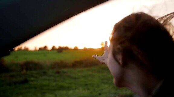 幸福-年轻女子在车里手在空中玩大自然中美丽的日落风吹头发缓慢的莫