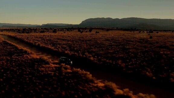 航拍:金色夕阳下黑色SUV吉普车行驶在沙漠山谷的土路上