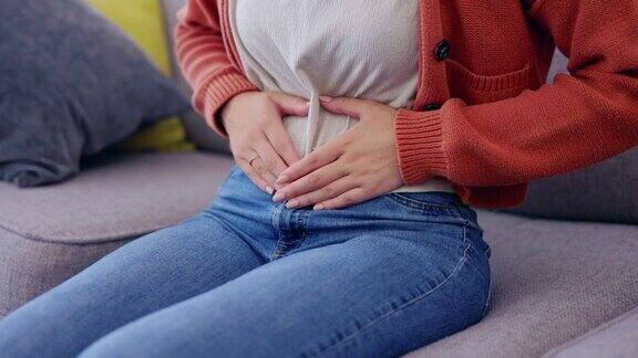 胃痛痉挛和女人手躺椅上消化和月经问题在家里的沙发上便秘肚子痛和腹部健康问题在一个房子在沙发上腹胀和肠胀