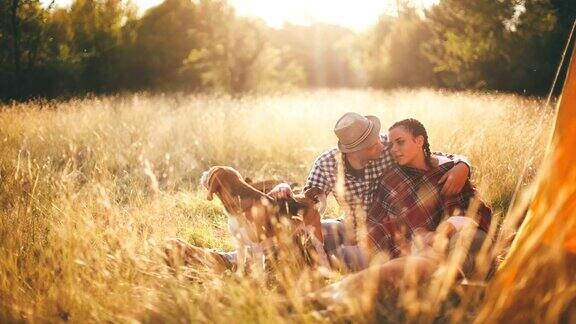 一对夫妇在浪漫的秋天露营时与他们顽皮的狗玩耍