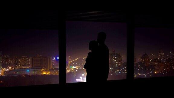 这对情侣在夜色中的城市背景下靠近窗户拥抱时间流逝