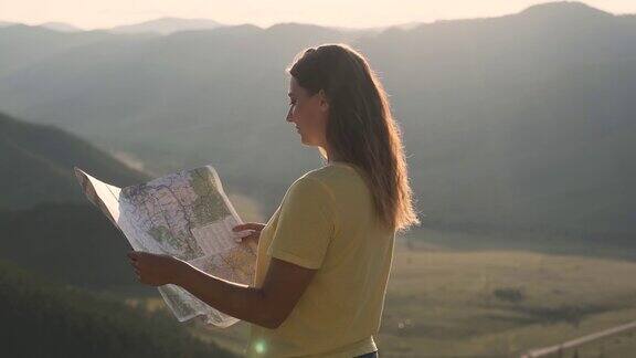 一名女游客站在悬崖边手里拿着地图寻找旅游路线