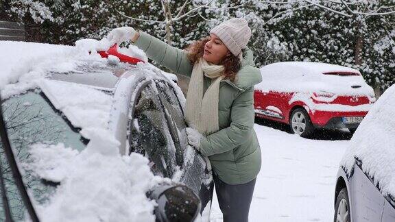 年轻女子正在清理车上的雪