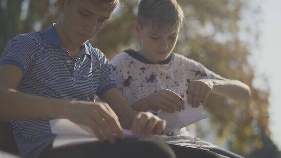 两个小男孩在户外做纸飞机孩子们坐在公园的长椅上