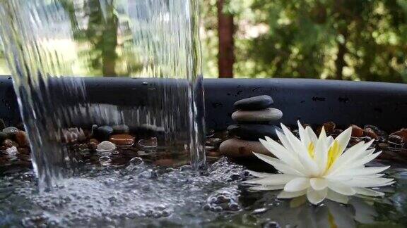 水在平衡石和白色睡莲花附近下落的慢动作