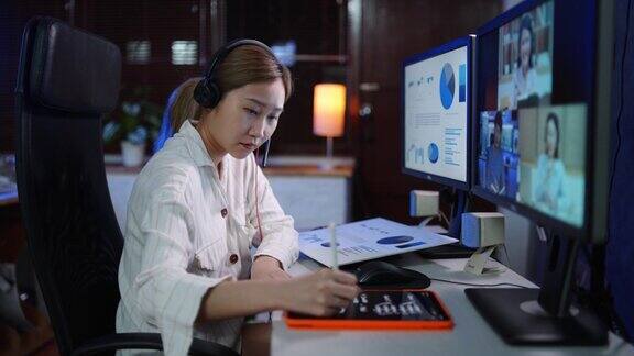 年轻的亚洲女性使用电脑视频电话的业务会议而工作到深夜在家里的办公室