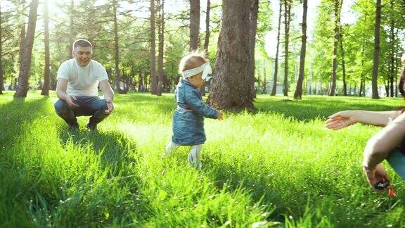 阳光明媚的公园草地上蹒跚学步的小女孩从父亲走向母亲的第一步