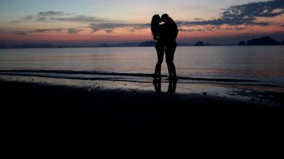 一对情侣在海滩上亲吻在日落男人和女人在水里牵手拥抱