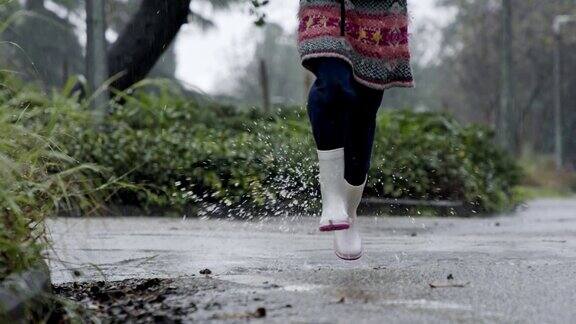 一个小女孩在水坑里抱着伞在雨中跳跃的慢动作