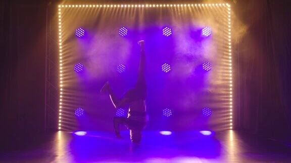 一个专业的男舞者表演倒立和头部旋转街舞霹雳舞在一个黑暗的工作室与蓝色的灯慢动作