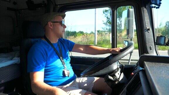 司机戴着墨镜坐在卡车的方向盘后在阳光明媚的乡村道路上行驶一个人控制着他的卡车注意观察道路卡车司机在车慢镜头