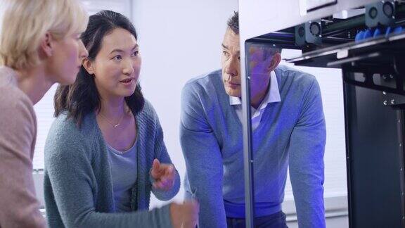 一位亚洲女工程师和他的两位同事正在研究3D打印机模型的构建并讨论其进展