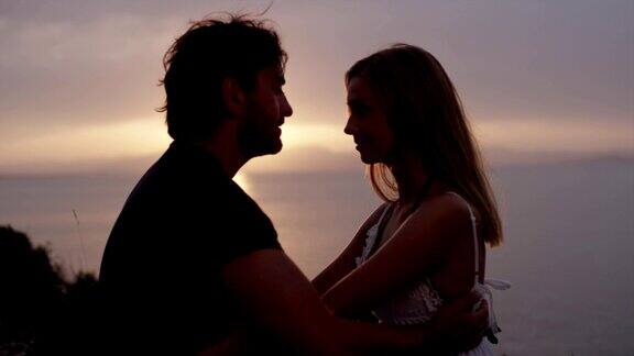 一对浪漫的情侣在岩石海岸拥抱日落