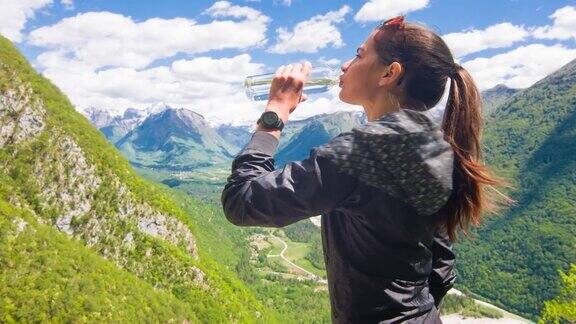 一位女徒步旅行者在一个阳光明媚的日子里一边喝着水一边欣赏着山景