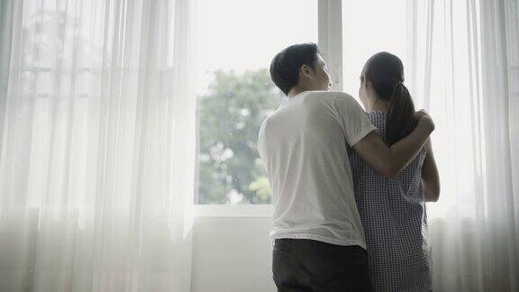 清晨一对年轻夫妇在窗前拥抱聊天