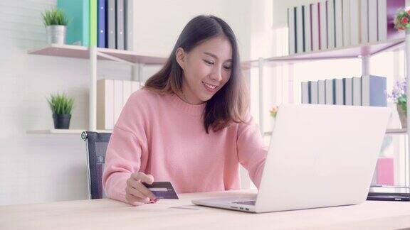 美丽的亚洲女人使用电脑或笔记本电脑购买网上购物的信用卡而穿着毛衣坐在家里客厅的桌子上生活方式女性在家