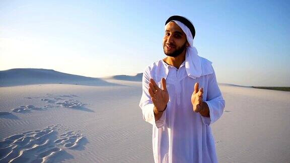 一个阿拉伯人站在广阔的沙漠中在夏日的空旷中看着镜头告诉我们信息和我们握手