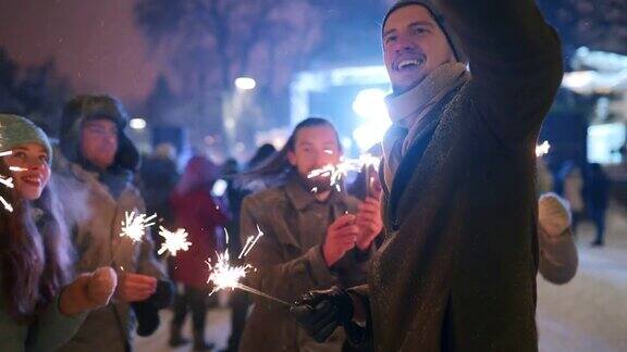 朋友们在圣诞市场上玩烟花用智能手机自拍冬夜人们在新年游乐场蹦蹦跳跳雪花灯泡花环的背景