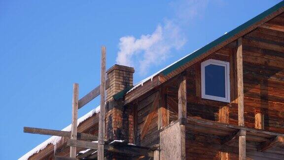 在蓝天的映衬下冬天木房子屋顶上的砖烟囱冒出的烟