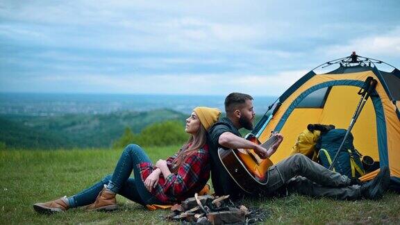 在大自然中几个露营者坐在帐篷附近弹吉他