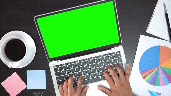 俯视图男性双手工作的笔记本电脑与绿色屏幕在白色的桌子上从上面