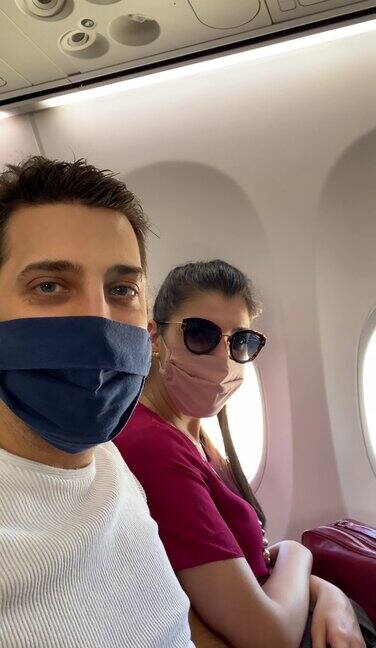 年轻的夫妇做一个视频电话与口罩在飞机上pov的移动屏幕