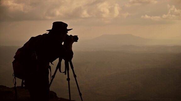剪影概念风景摄影师在日落时拍摄山的照片
