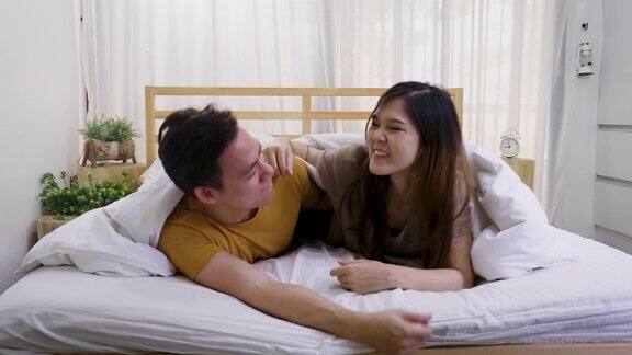 年轻的亚洲幸福夫妇躺在床上盖着毯子在家里玩耍睡觉