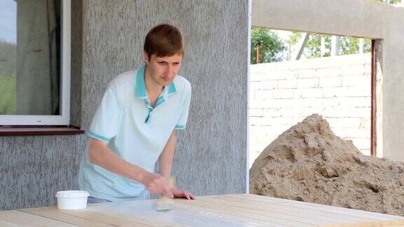 年轻人正在把一张木桌漆成白色