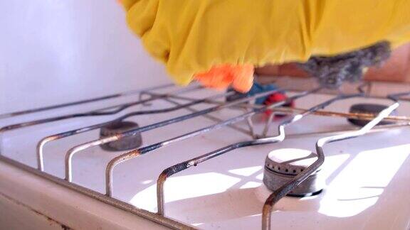 女人戴着黄色橡胶手套的手在厨房洗脏煤气炉
