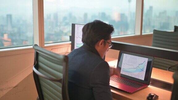 亚洲华人中年人看着笔记本电脑与图表在他的工作场所的压力
