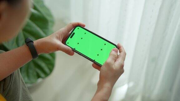 女人拿着智能手机横向滚动着绿色屏幕坐在客厅里