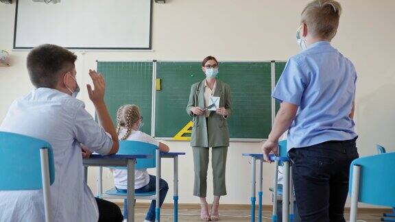 戴面具的老师站在教室前面向学生展示印有字母的卡片学生们在课堂上专心听讲并举手
