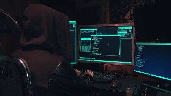 带着兜帽的黑客坐在电脑屏幕前侵入数据库