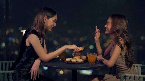晚上4K亚洲女性朋友在摩天大楼的屋顶餐厅吃晚餐喝鸡尾酒