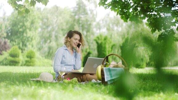 在野外野餐时用笔记本电脑打电话的女人