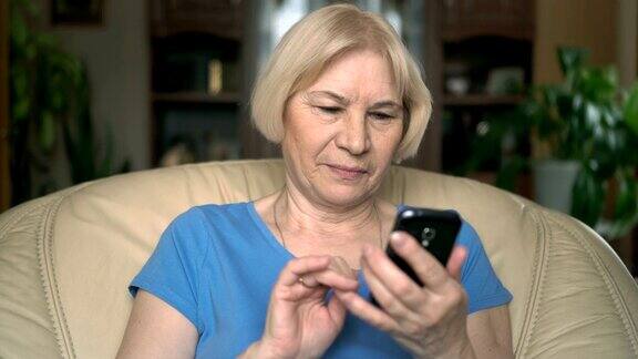 开朗漂亮的老年妇女坐在家里的椅子上用她的智能手机浏览
