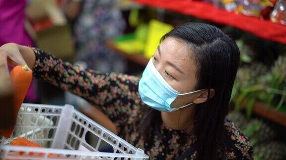 年轻的亚洲妇女戴着保护面罩在超市选购胡萝卜