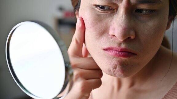 一名亚洲女性通过迷你镜看到脸上出现痘痘和皱纹后开始担心自己的脸