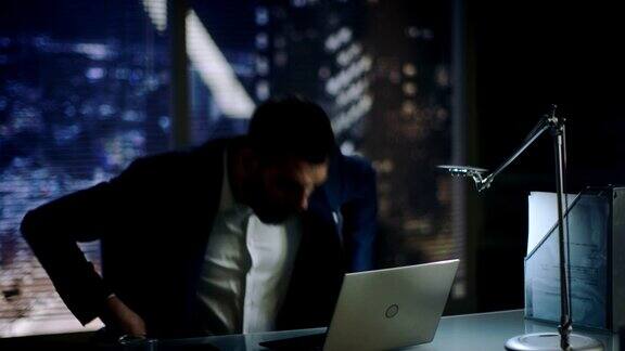 深夜商人站在他办公室的窗户前可以看到大城市的景色然后他坐在办公桌前开始用笔记本电脑工作
