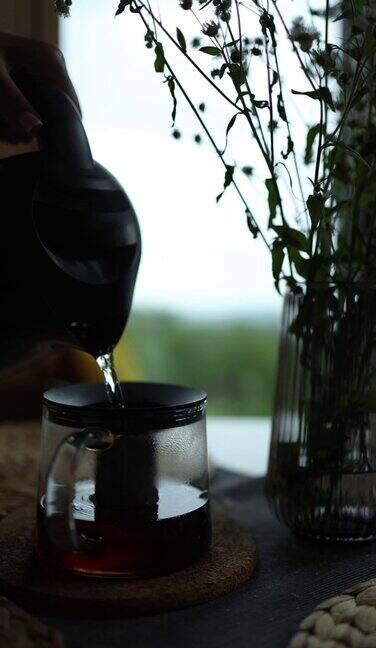 在下着雨的窗户背景上泡茶女手将开水倒进家里桌子上的茶壶里垂直视频
