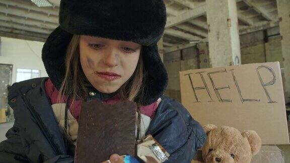 一个无家可归的白人女孩的肖像肮脏的脸和灰色的眼睛贪婪地吃巧克力棒