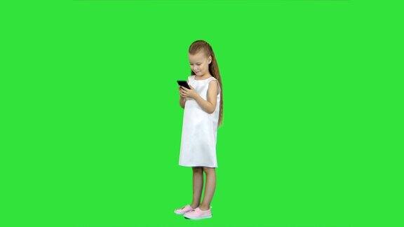 可爱的小女孩微笑着用绿色屏幕上的手机色度键